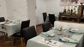 Un espace repas avec des tables préparées pour deux personnes, agrémenté de nappes blanches et de chaises noires.