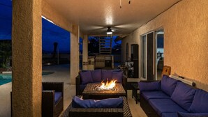 Ein Außenbereich mit Terrasse, Feuerstelle, Sitzgelegenheiten und Deckenventilator.