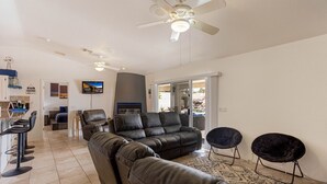 Ein modernes Wohnzimmer mit einem schwarzen Ledersofa, zwei schwarzen Sesseln, einem Deckenventilator und Blick ins Freie.
