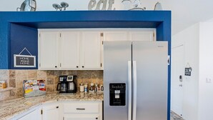 Eine moderne Küche mit weißen Schränken, einem Edelstahl-Kühlschrank, einer Kaffeemaschine und einem Wasserspender.