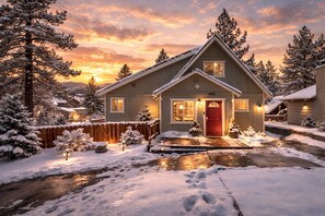 Une maison à deux étages avec une porte rouge, entourée d’arbres couverts de neige et d’une clôture en bois.