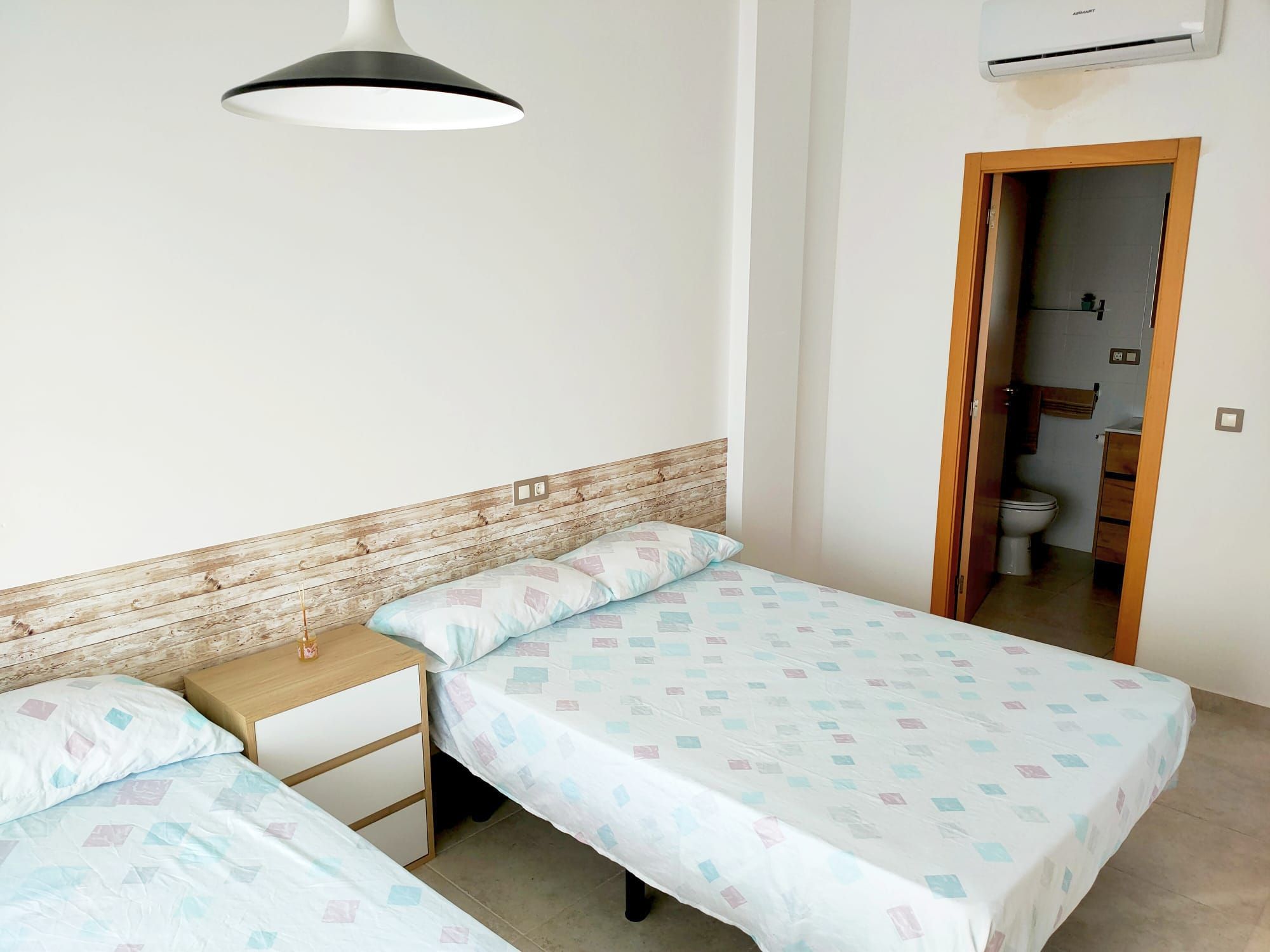 Un dormitorio con dos camas individuales, cabecero de madera, mesita de noche y lámpara colgante.