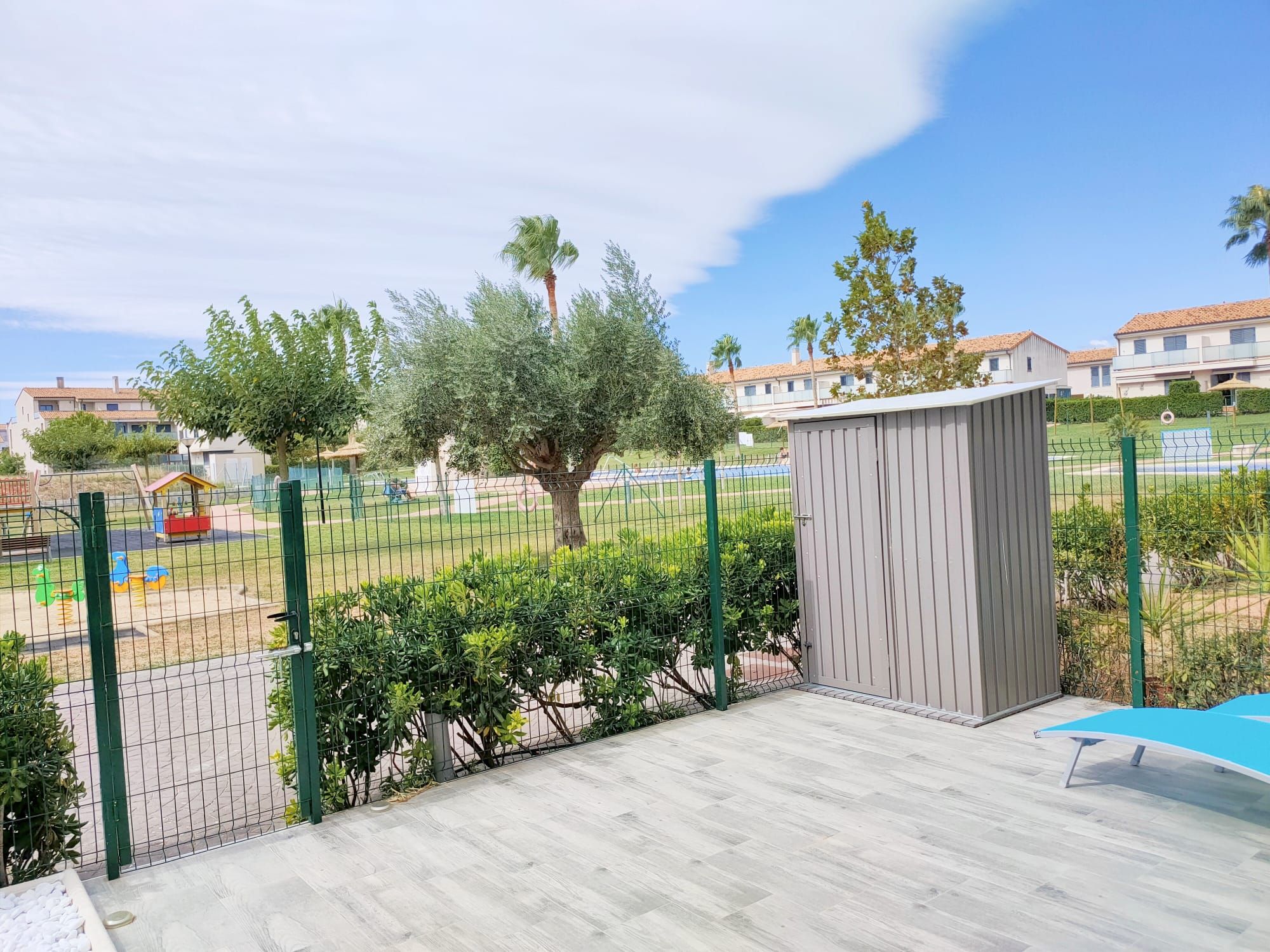 A fenced outdoor area with a wooden deck, a small shed, and a playground with colorful equipment.