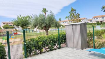A fenced outdoor area with a wooden deck, a small shed, and a playground with colorful equipment.