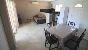 Een ruimtelijk ingerichte leefruimte met een eettafel, stoelen, een bank, een wasmachine en een kitchenette.