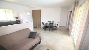 Een woonkamer met een bank, een koffieapparaat, een eettafel met stoelen en een raam met gordijnen.