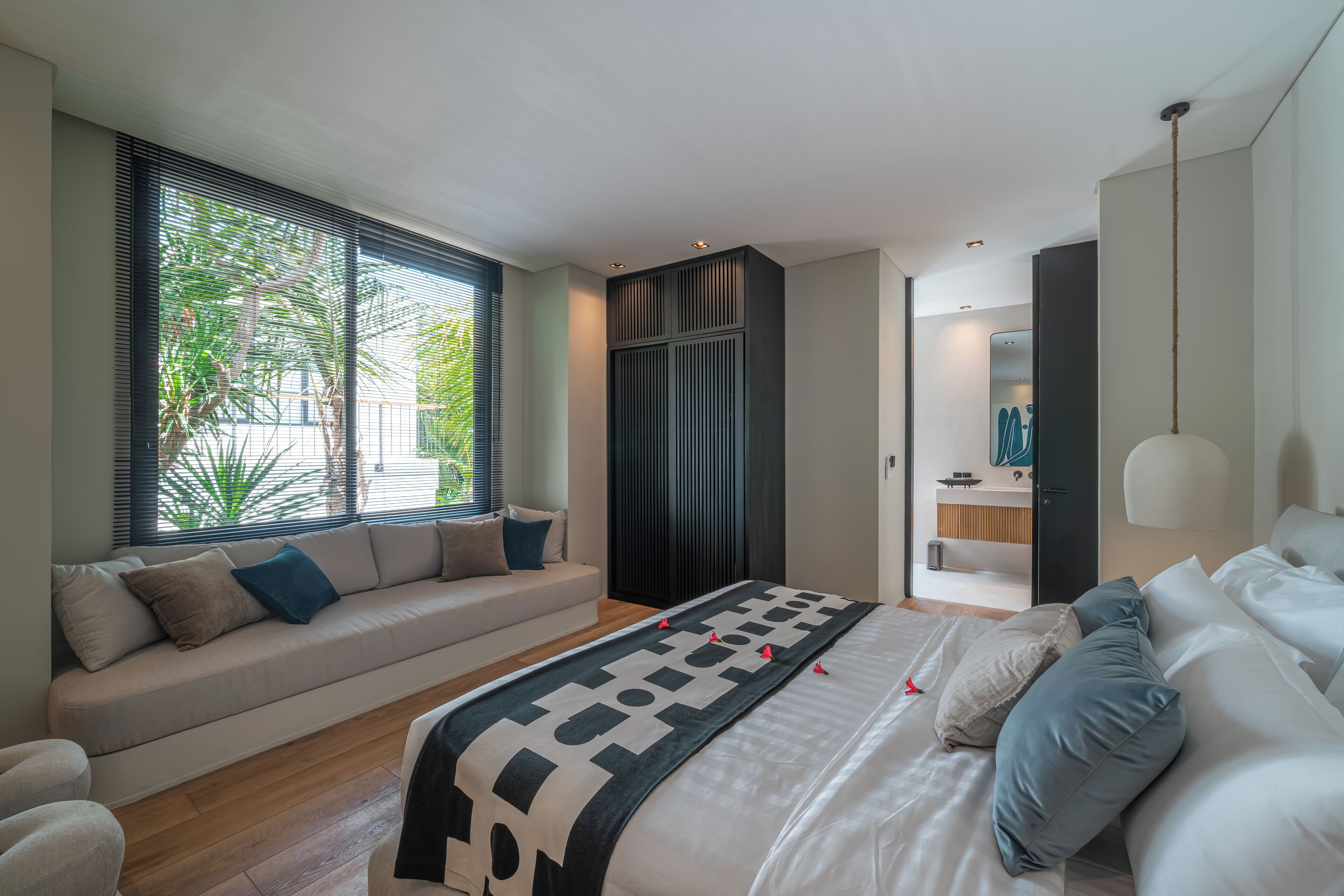 A modern bedroom with a large bed, a sofa, and a view of the outdoors through large windows.