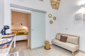 A modern living room with a sofa, a dining table with breakfast items, a small wooden stool, and a door leading to a bedroom.