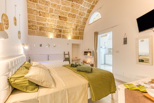 A bedroom with a stone ceiling, a bed with green and white bedding, a white dresser, and a television mounted on the wall.