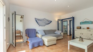 A living room with a sofa, ottoman, and a coffee table. There is a door leading to another room, and a sign on the wall that says 'BEACH'.