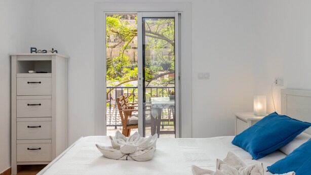 A bedroom with a bed, a nightstand, a dresser, and a balcony with a table and chairs.