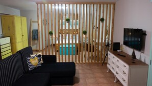 Un salon comprenant un canapé, un téléviseur, une commode blanche et une cloison en bois agrémentée de plantes.