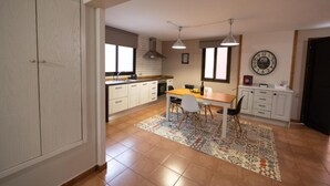 Une cuisine avec des meubles blancs, une table à manger avec des chaises, un tapis à motifs et une horloge au mur.