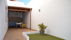 Une petite terrasse avec une table et des chaises, une plante en pot et, au fond, un mur recouvert de carreaux.