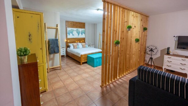 Une chambre avec un lit, une cloison en bois, un ventilateur et un téléviseur.