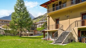 Un edificio con una escalera que lleva a un balcón, rodeado de césped, árboles y una montaña al fondo.