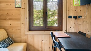 Interior de una cabaña de madera con un ventanal grande, una cama, una mesa y un televisor montado en la pared.