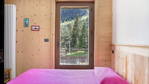 Une chambre avec une porte en bois, une couvre-lit rose et une vue sur une forêt par la fenêtre.