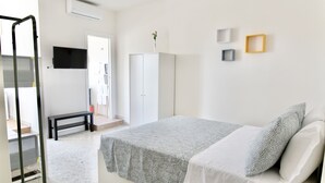 Ein Schlafzimmer mit Bett, Kleiderschrank, einer Bank und einem Fernseher an der Wand.