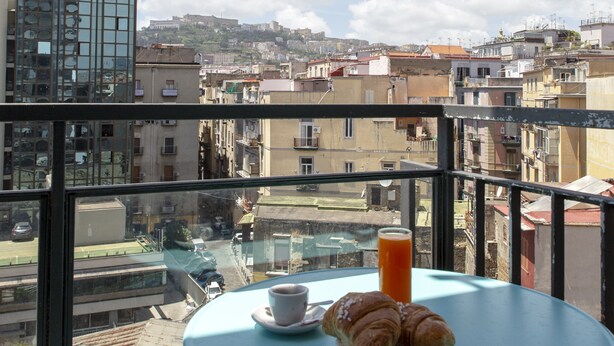 Ein Balkon mit Tisch, einem Croissant, einer Tasse und einem Glas Orangensaft.