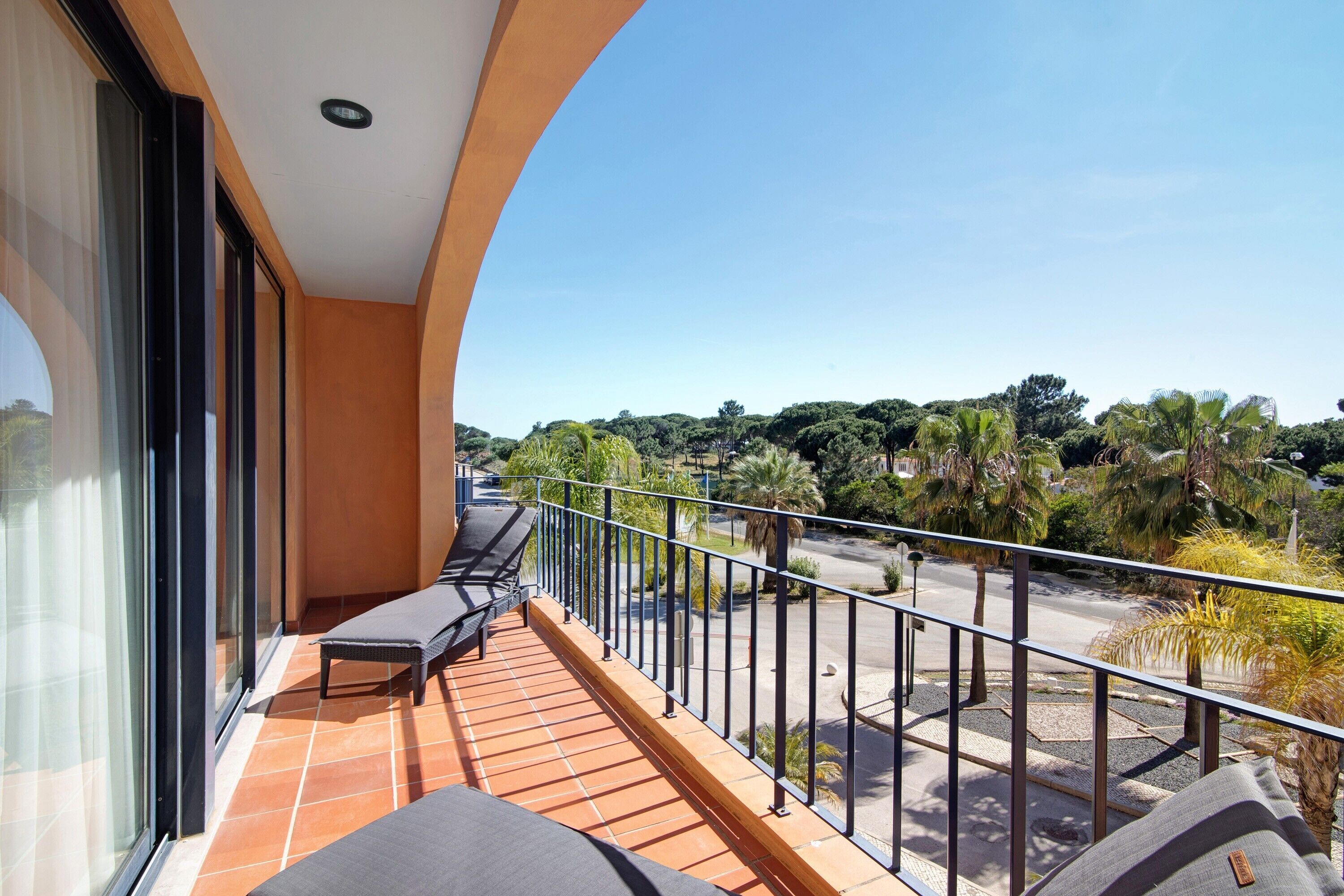A balcony with a view of a road and greenery, a glass door, and a small seating area.
