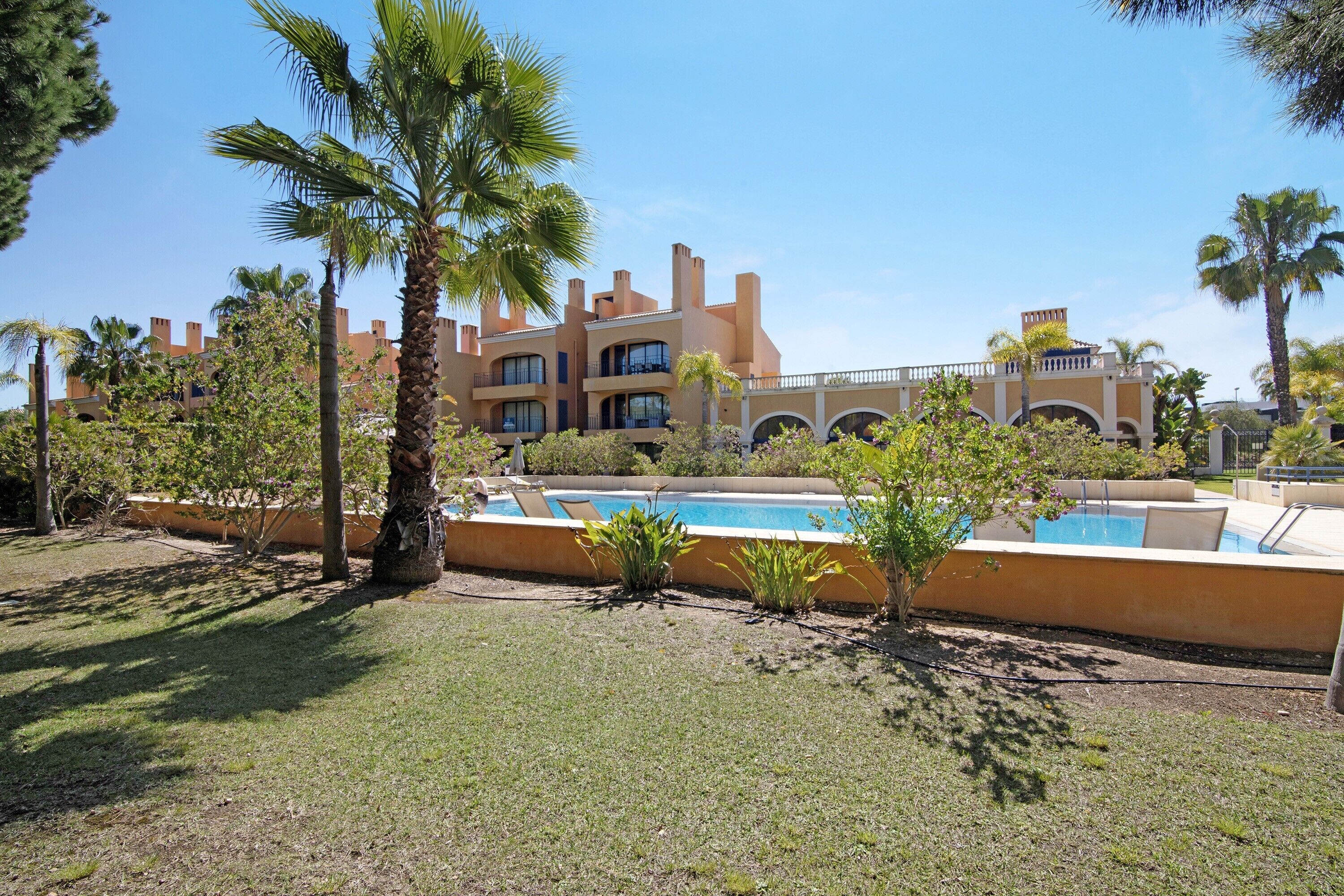 A resort with a pool, palm trees, and a large building with multiple balconies.