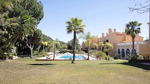 A pool area with palm trees, a building with arches, and a clear sky. - Apartment "T2 Vilasol" with Shared Pool & Wi-Fi (Vilamoura)