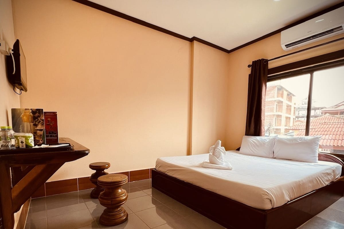 Een hotelkamer met een bed, een bureau, een stoel, een prullenbak en een airconditioning.