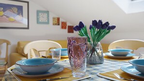 Una mesa de comedor dispuesta con platos azules, una copa de cristal transparente y tulipanes morados en un florero.