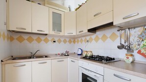 Una cocina con armarios blancos, estufa a gas, lavamanos y salpicadero de azulejos.