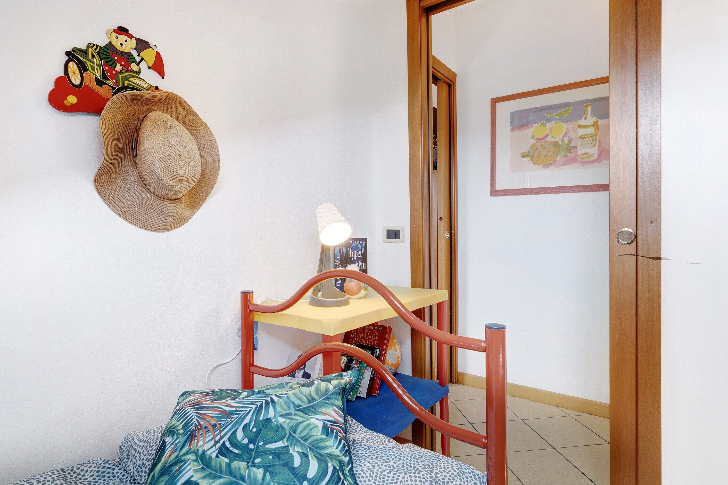 A bedroom with a bed, a nightstand, a lamp, a wall clock, a door, and a wall decoration.