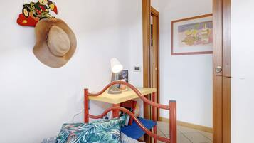 A bedroom with a bed, a nightstand, a lamp, a wall clock, a door, and a wall decoration.