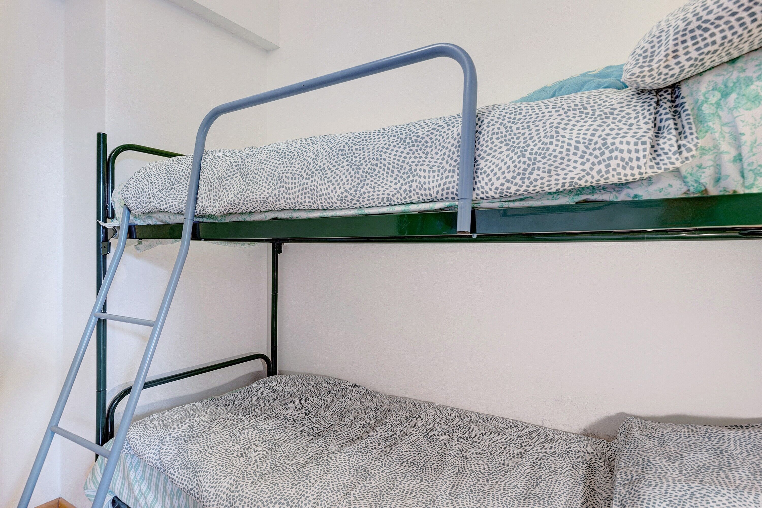 Un lit superposé avec une échelle, un coussin à motifs et un mur uni.