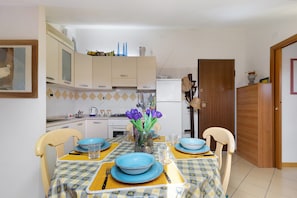 Un coin repas avec une table dressée pour quatre personnes, des chaises, un vase avec des fleurs et, au fond, des meubles de cuisine.