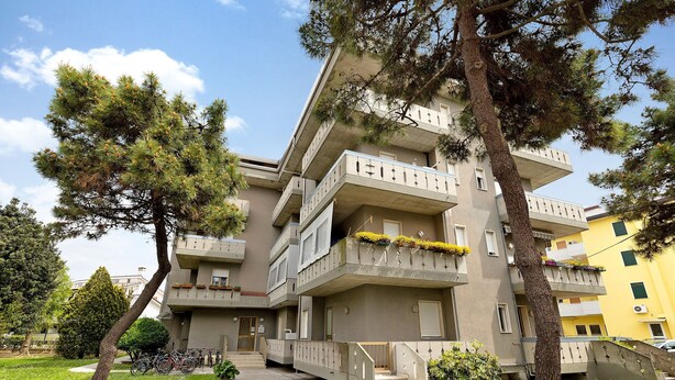 Un edificio residencial de varios pisos con balcones, una escalera central y un área verde circundante.
