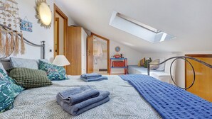 Un dormitorio con techo inclinado, una cama con ropa de cama estampada, una mesita de noche y vistas al baño.