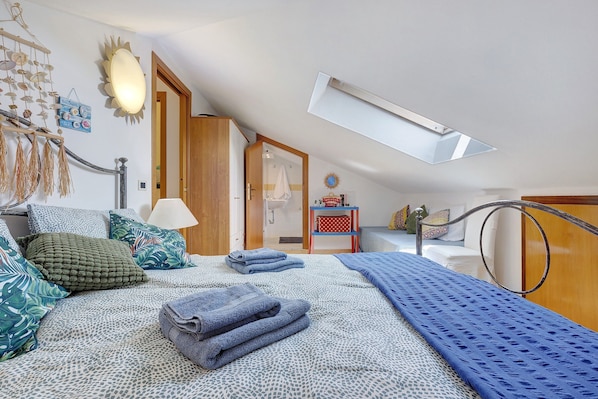 Une chambre avec un plafond en pente, un lit avec une literie à motifs, une table de chevet et une vue sur la salle de bain.