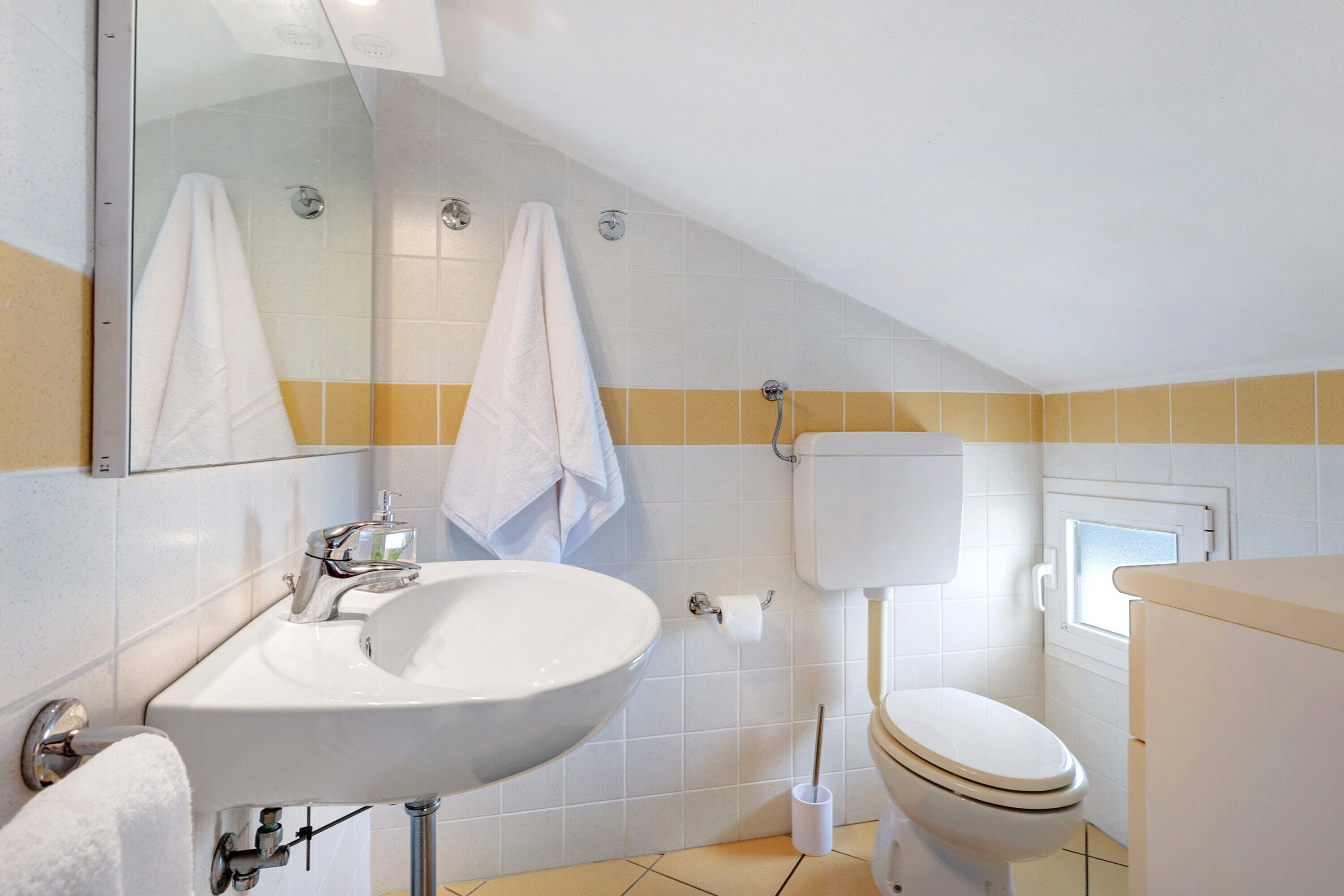 Une salle de bain avec un lavabo blanc, des toilettes et un miroir au-dessus du lavabo.