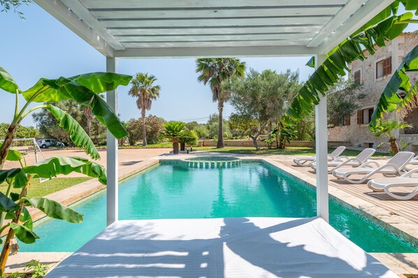 Ein Poolbereich mit einer Pergola, Liegestühlen und Palmen.