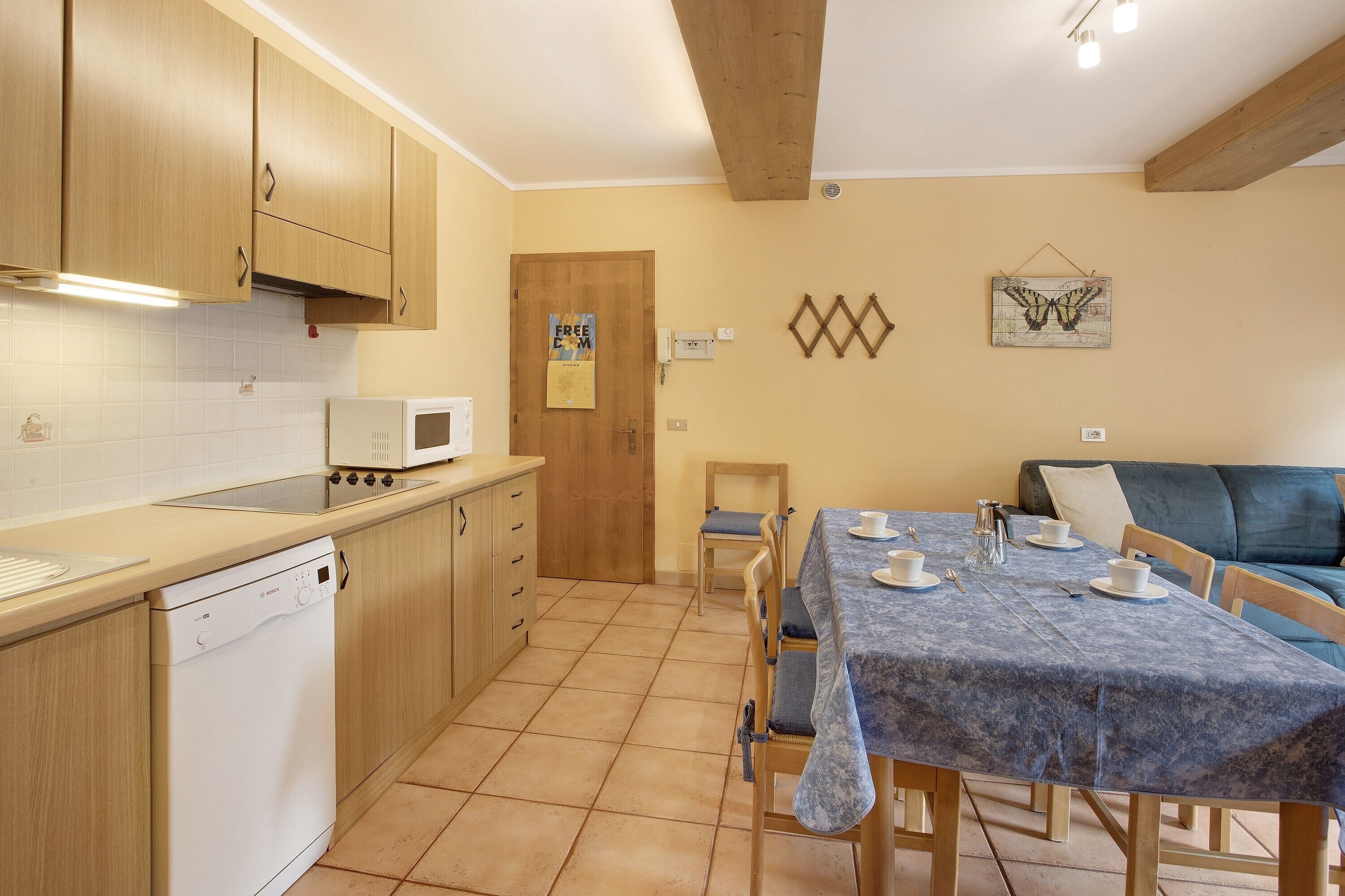 A kitchen with wooden cabinets, a dishwasher, a microwave, and a dining area with a table set for two.