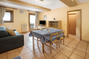 A living room with a sofa, a dining table with chairs, a TV, and a wooden door.