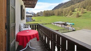 Ein Balkon mit Tisch und Stühlen, mit Blick auf ein grünes Feld und Berge.