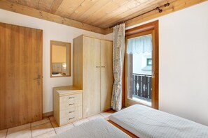 A bedroom with wooden ceiling, a wardrobe, a bedside table, a bed, a window with a view, and a balcony.
