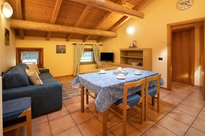 Una zona d'estar acollidora amb un sofà, una taula de dinar amb cadires, una televisió i un sostre de fusta.