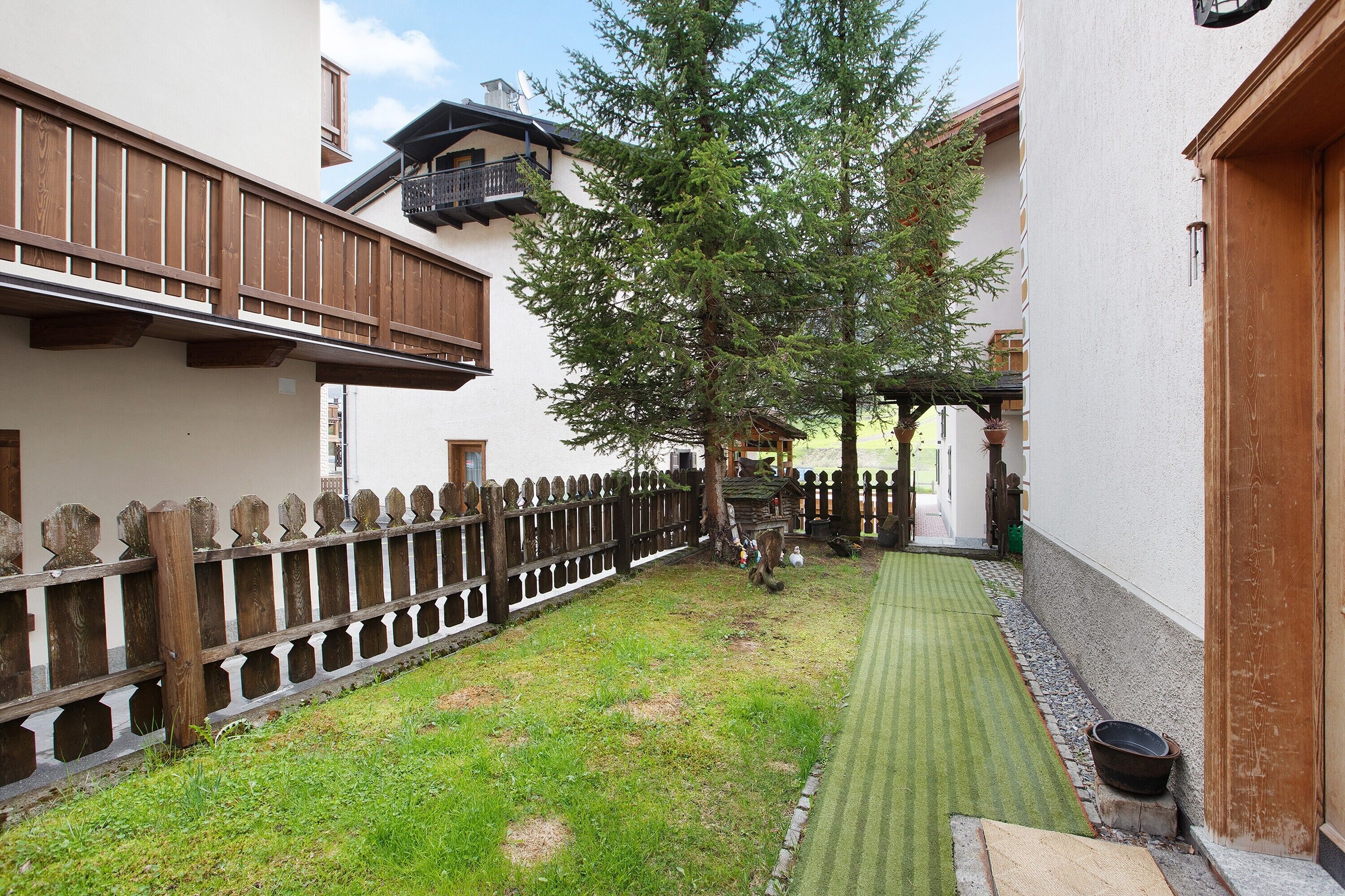 A courtyard with a wooden fence, a tree, and a green lawn.