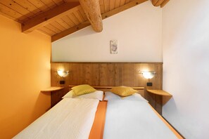 Une pièce avec un plafond en bois, un lit avec une literie blanche, deux tables de chevet et des lampes fixées au mur.