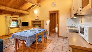 Un coin repas avec une table dressée pour quatre personnes, des meubles en bois, une cuisine équipée d’un four à micro-ondes et un téléviseur placé dans un coin.