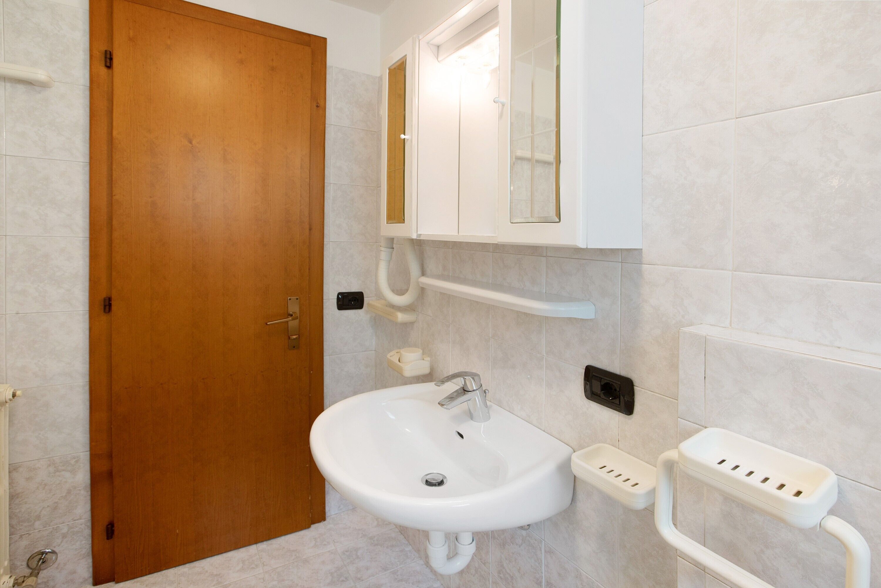 Une salle de bain avec une porte en bois, un lavabo blanc avec un miroir au-dessus, et un porte-serviettes.