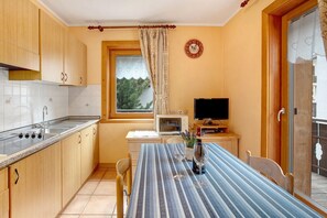 A compact kitchen with a microwave, stove, and sink, a dining table with chairs, a TV, and a window with a view of trees.