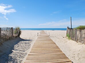 A wooden boardwalk leading to a sandy beach with a clear blue sky.